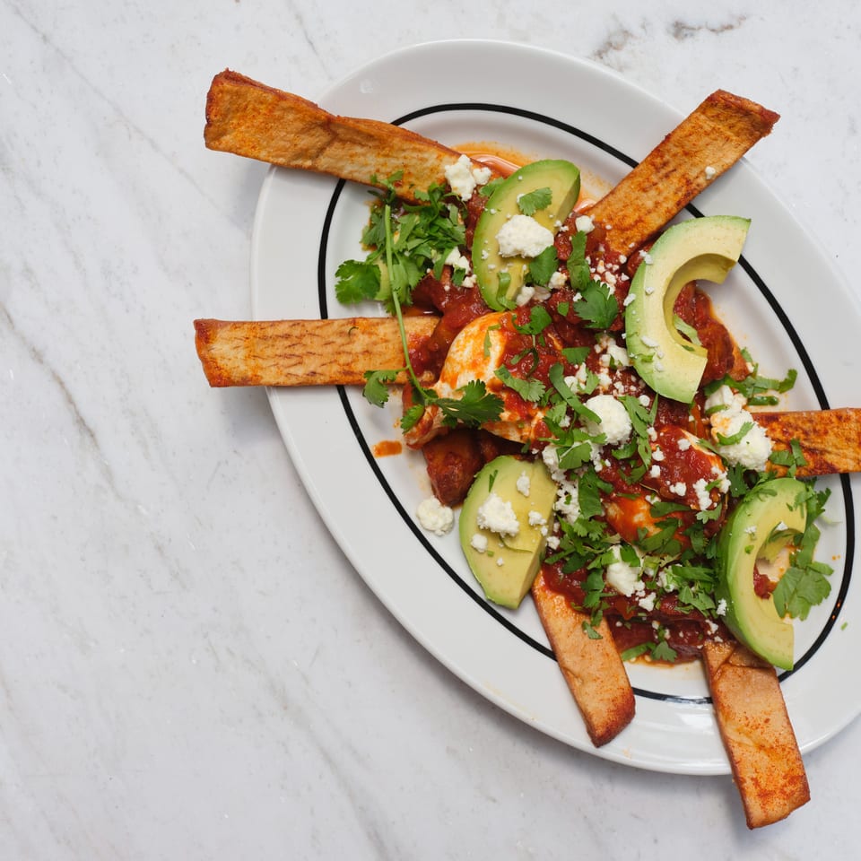 Overhead view of crispy tortilla strips topped with red salsa, avocado slices, cilantro, and crumbled cheese on a white plate.