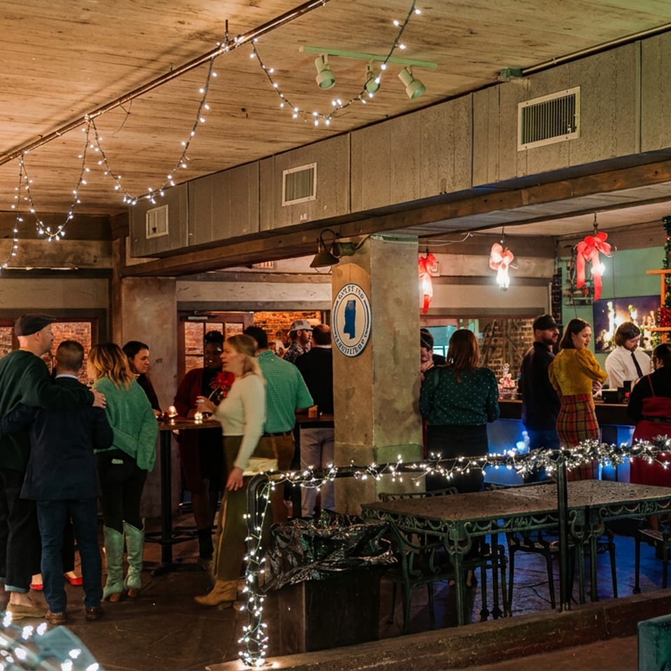 Guests mingle in a warmly lit bar area decorated with string lights and festive garlands.
